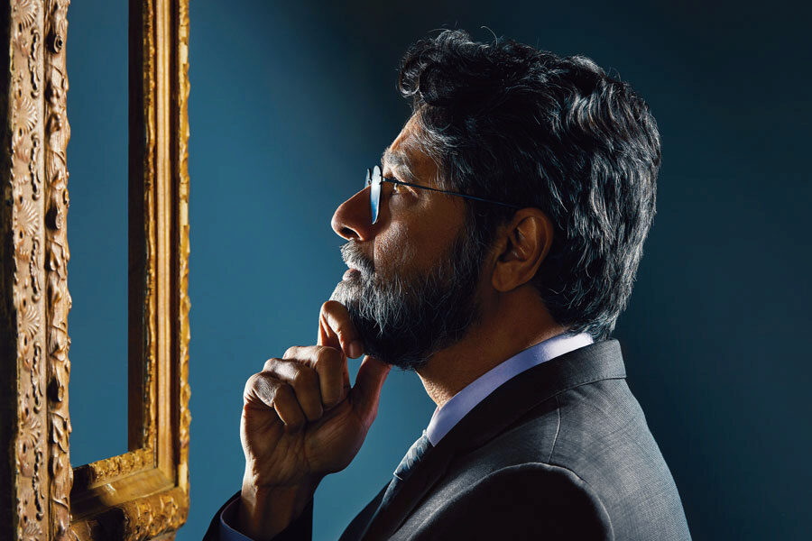 penn-center-for-neuroaesthetics A person in a suit looks thoughtfully at a framed piece of art, with light illuminating their face.