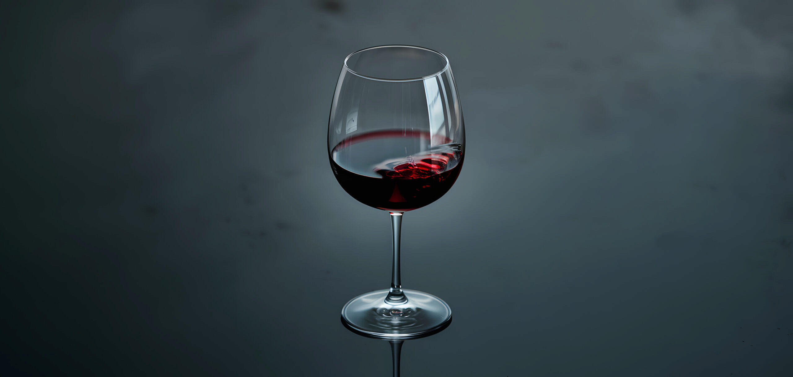 A glass of red wine on a reflective surface with a dark, moody background.