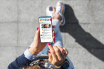 A person holding a smartphone displaying a social media app with several messages. They are sitting outdoors, wearing casual clothes and sneakers.