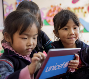 Screen Shot 2024-10-29 at 8.01.19 PM A small group of children interacting with a tablet displaying the UNICEF logo, suggesting a focus on education and technology.