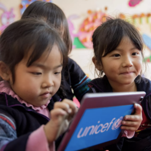 A small group of children interacting with a tablet displaying the UNICEF logo, suggesting a focus on education and technology.