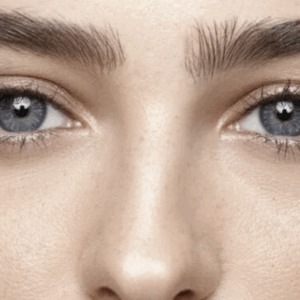 Close-up of a person's eyes with blue irises, surrounded by dark eyebrows and smooth skin.